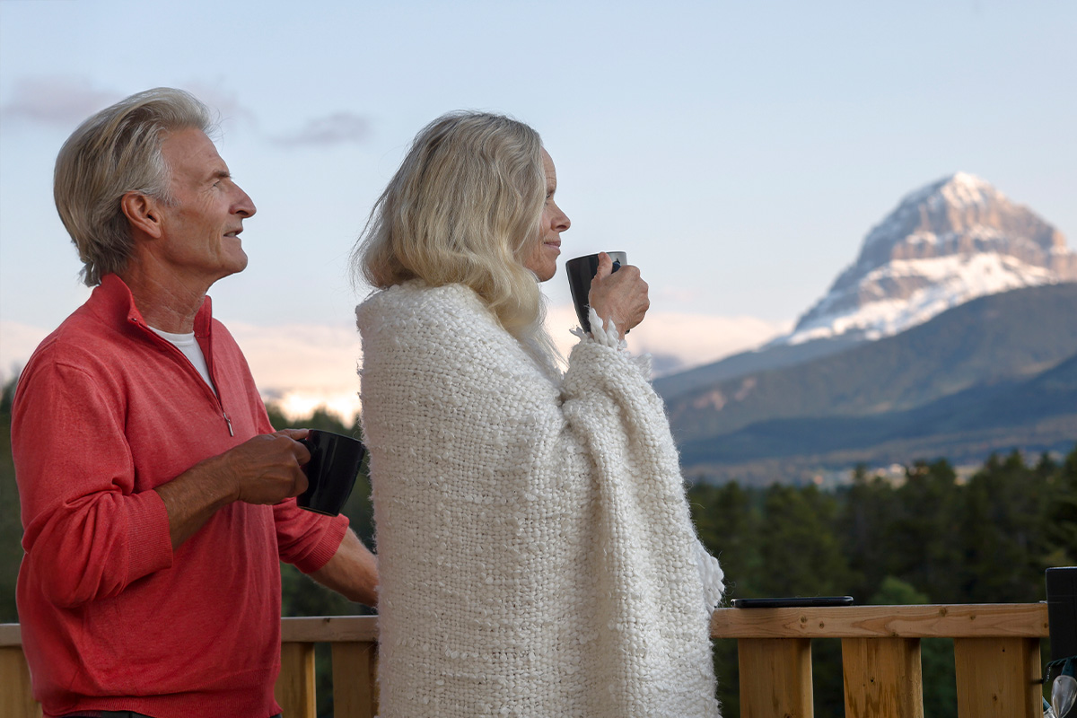 Pareja mayor disfrutando de un café en un balcón con vista a un paisaje de montañas.