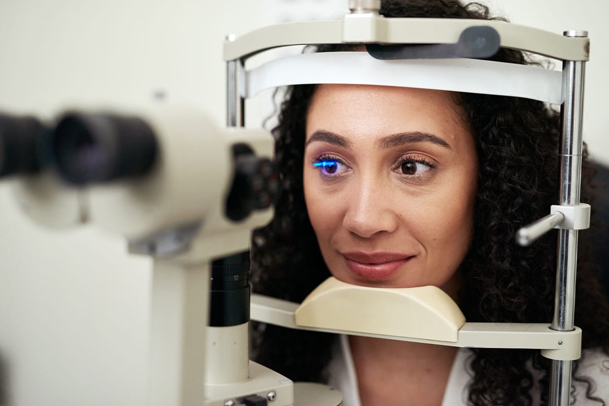 Woman undergoing a slit lamp eye exam with blue diagnostic light at an eye clinic.