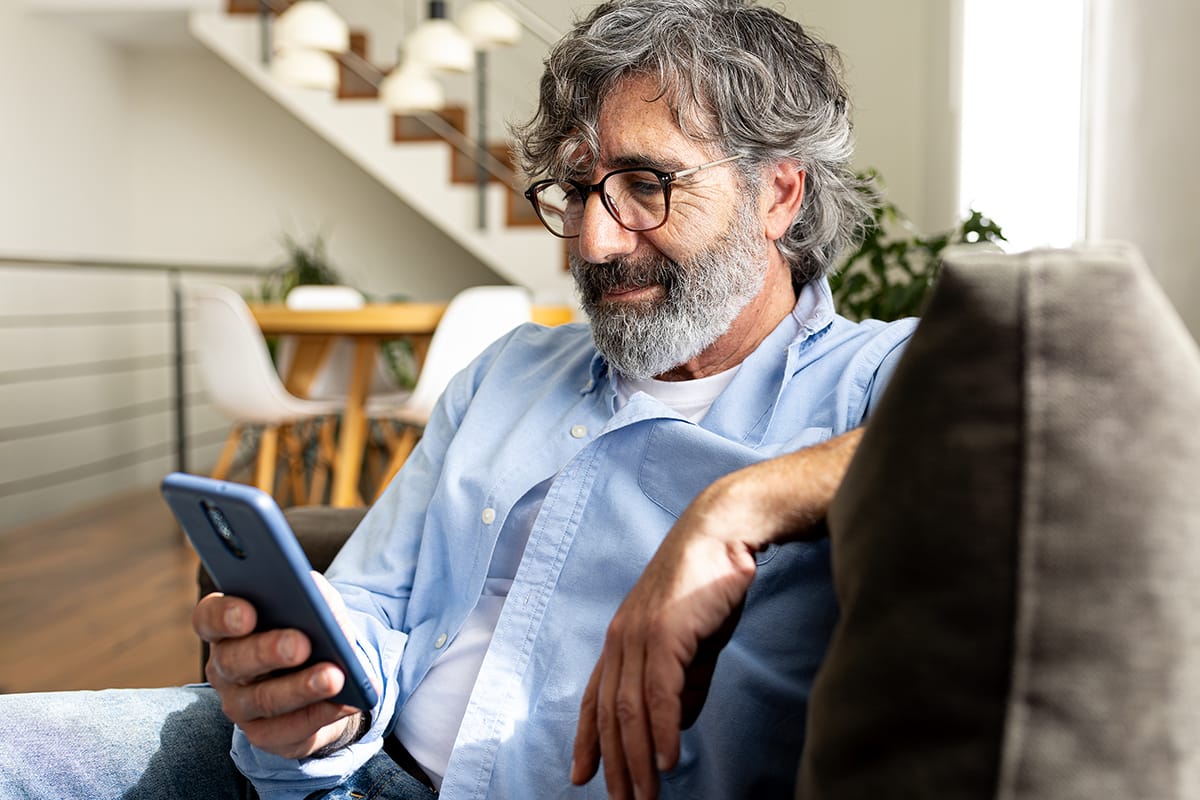 Hombre mayor con lentes leyendo en un teléfono inteligente en casa.