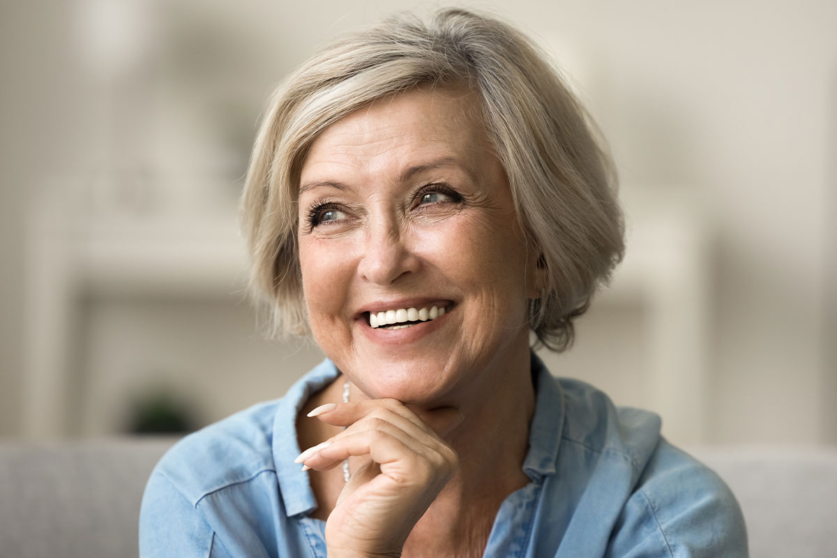 Smiling older woman with short gray hair looking off to the side in a relaxed indoor setting.