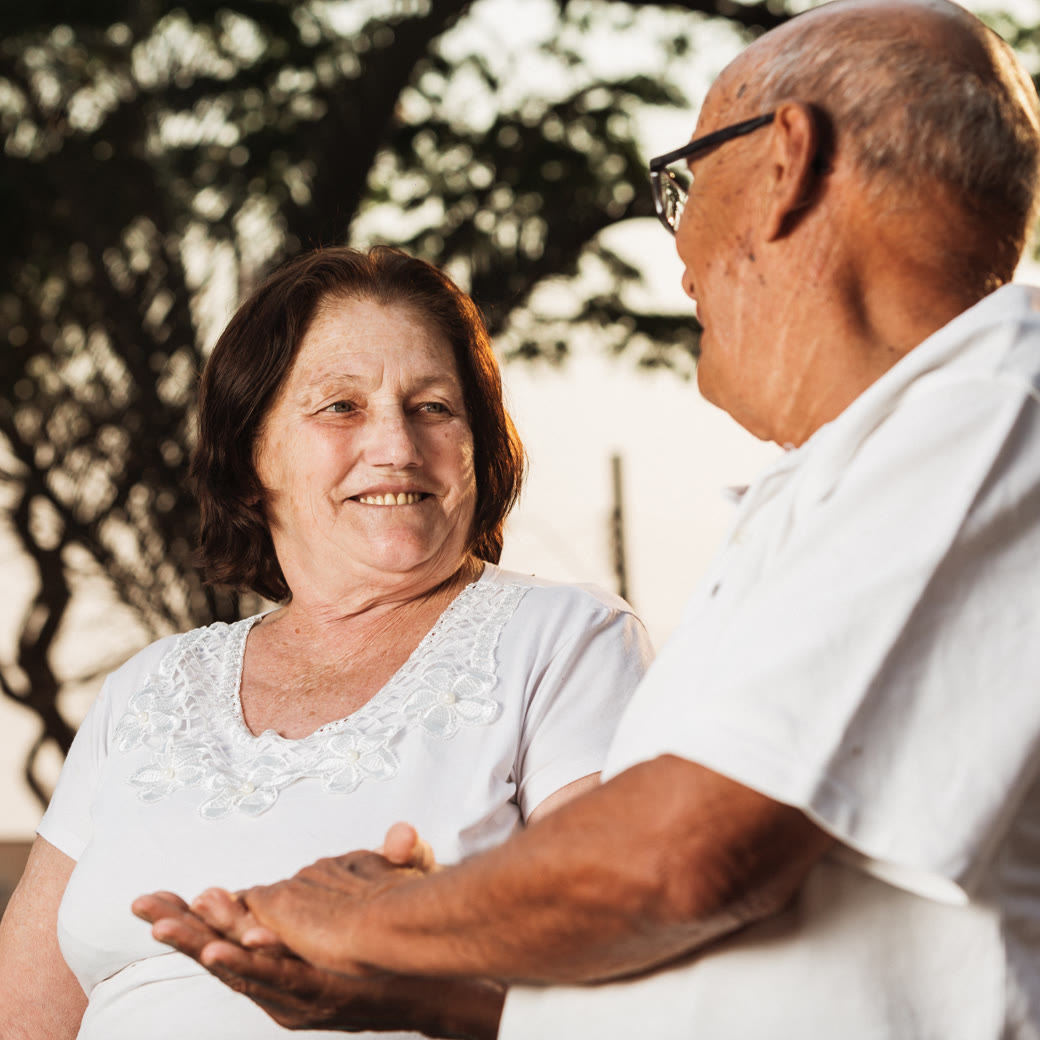 Pareja de adultos mayores tomados de las manos, sonriendo bajo la luz del atardecer